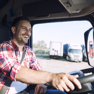 Truck driver job. Middle aged trucker driving truck. Professional middle aged truck driver in casual clothes driving truck vehicle and delivering cargo to destination. Transportation service.